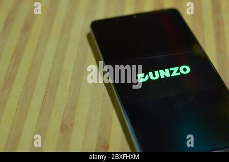 Nuova Delhi, India, 2020. Logo dell'app Flat Lay Dunzo Delivery illuminato sullo schermo del telefono cellulare su sfondo in legno. Messa a fuoco selettiva e profondità ridotta Foto Stock