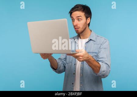Ritratto di uomo divertente in camicia di jeans lavoratore guardando lo schermo del laptop con stupito espressione, guardando contenuti scioccanti, sorpreso da errore software. io Foto Stock