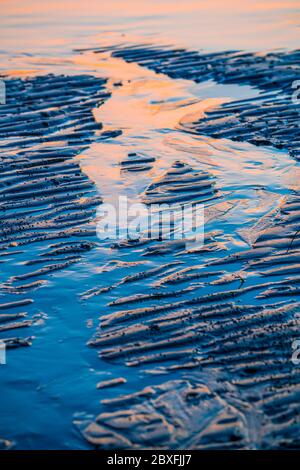 Increspature e riflessi sulla sabbia bagnata della spiaggia alla luce del mattino presto Foto Stock