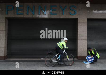 Il sergente di Garda Rodger Quinn (a sinistra) parla al lavoratore del consiglio comunale di Dublino, Joe Carroll, mettendo in coda gli adesivi su o'Connell Street, fuori Penneys a Dublino, prima della sua riapertura, poiché la seconda fase della mappa stradale irlandese per il recupero dei coronavirus inizierà lunedì come previsto, insieme ad altre misure originariamente previste per le fasi successive. Foto Stock