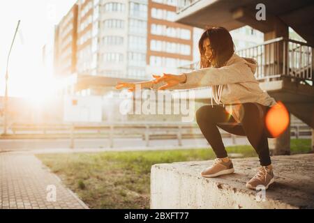 Adatta giovane donna facendo esercizi a squadre con fitness gum all'aperto in ambiente urbano sotto il ponte. Ragazza slim-fit che si allunga all'esterno al tramonto Foto Stock