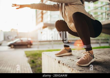 Adatta giovane donna facendo esercizi a squadre con fitness gum all'aperto in ambiente urbano sotto il ponte. Ragazza slim-fit che si allunga all'esterno al tramonto Foto Stock