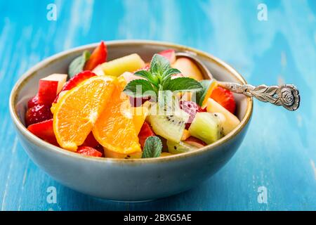 Macedonia di frutta fresca piena di vitamine per l'estate con menta su sfondo blu Foto Stock