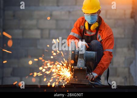 Operatore industriale che indossa una maschera facciale che taglia il metallo con una smerigliatrice metallica Foto Stock