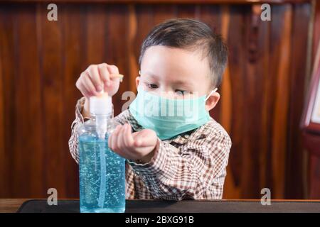 Ragazzo che indossa una maschera chirurgica utilizzando un disinfettante per le mani Foto Stock