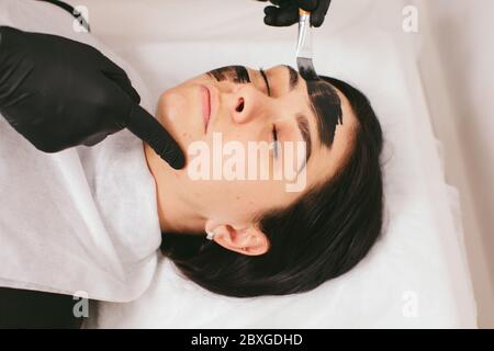 Estetista preparando una donna per un trattamento di bellezza con buccia di carbonio in una clinica Foto Stock