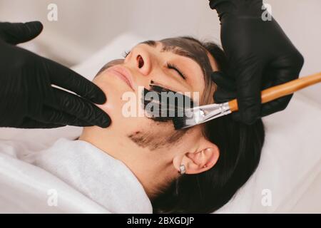 Estetista preparando una donna per un trattamento di bellezza con buccia di carbonio in una clinica Foto Stock