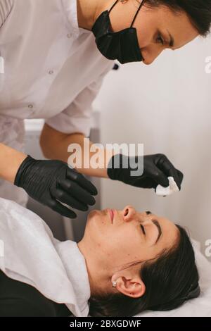 Estetista che pulisce il viso di una donna dopo un trattamento di bellezza con buccia di carbonio Foto Stock