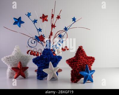 Stelle di colore rosso, bianco e blu e stelle di glitter su un bancone bianco con uno spray decorativo di nastro arricciato e stelle dietro di esso per il 4° di J. Foto Stock