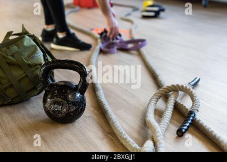 Preparazione di attrezzature per palestra per il campo di stivali e allenarsi con il bicchiere, la corda, il sacco di sabbia nella palestra sul pavimento. Gambe dell'istruttore sullo sfondo. Foto Stock