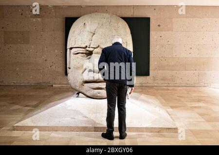 Un turista si affaccia su una colossale testa di pietra Olmec presso il Museo di Antropologia nel centro storico di Xalapa, Veracruz, Messico. La civiltà Olmec fu la prima civiltà mesoamericana conosciuta, che risale approssimativamente dal 1500 a.C. a circa 400 a.C.. Foto Stock