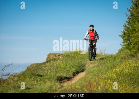 Donna anziana che cavalca la sua mountain bike elettrica sulle montagne sopra Oberstaufen, Alpi Allgau, Baviera Germania Foto Stock