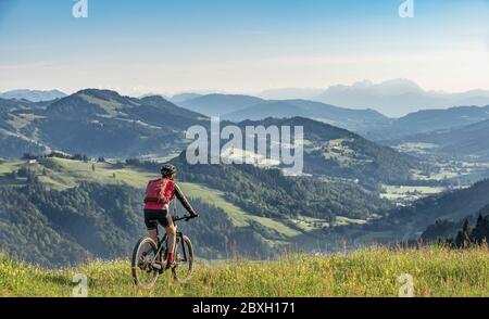 Bella donna anziana che cavalcava la sua mountain bike elettrica sopra Oberstaufen con una vista spettacolare sul Valdo di Bregenz, sulle Alpi di Allgau, in Baviera Germania Foto Stock