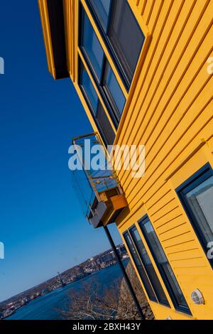 La parete esterna laterale di un edificio di legno placcato giallo luminoso con finestre chiuse e un patio di vetro. Il cielo blu luminoso e' sullo sfondo. Foto Stock