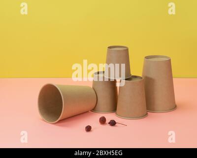 Tazze monouso e bacche di rosa selvatica su sfondo giallo e rosa. Utensili da cucina ecologici. Foto Stock