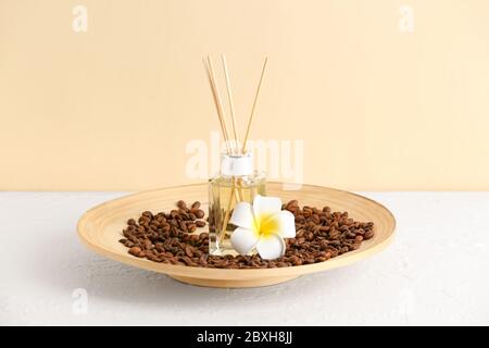 Piatto con diffusore a lamelle, chicchi di caffè e fiore sul tavolo Foto Stock