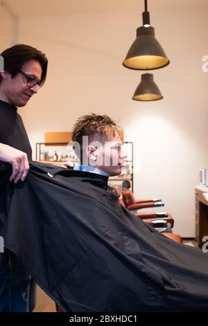 Barber altala il capo sopra il giovane uomo nel suo barbiere, pronto per un taglio di capelli Foto Stock