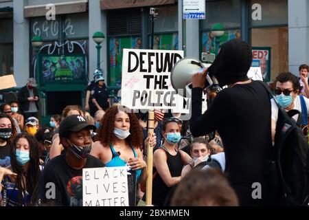 New York, New York. 6 giugno 2020. La gente ha segni compreso 'Defund la polizia' mentre una persona parla ad una folla attraverso un megafono ad una marcia di solidarietà della materia di vite nere attraverso Manhattan che chiede la giustizia in una serie recente di uccisioni americane della polizia: George Floyd, Breonna Taylor e ad innumerevoli altri. Migliaia di persone si sono unite alla marcia di protesta da Brooklyn che paralizzava Manhattan. 6 giugno 2020 Foto Stock