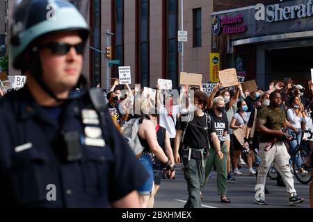 New York, New York. 6 giugno 2020. Persone che hanno segni, alcuni che tengono le mani in su in una posizione 'mani su non sparare' a una Black Lives materia solidarietà marcia attraverso Manhattan chiedendo giustizia in una serie recente di assassini della polizia americana: George Floyd, Breonna Taylor, e a innumerevoli altri. Migliaia di persone si sono unite alla marcia di protesta da Brooklyn che paralizzava Manhattan ben oltre un coprifuoco emesso all'inizio della settimana per frenare burglaries organizzati e saccheggi. Un poliziotto in un casco di rivolta cammina lungo il gruppo. 6 giugno 2020 Foto Stock