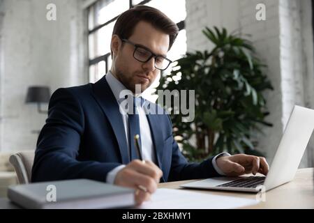 Serio datore di lavoro caucasico che lavora facendo note in ufficio Foto Stock