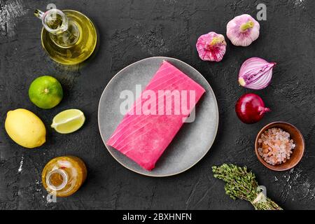 Vista dall'alto del filetto di tonno crudo in piastra con spezie su sfondo nero Foto Stock