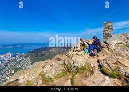 Persone che si siedono su rocce che guardano una vista panoramica dalla cima del monte Ulriken a Bergen, Norvegia Foto Stock