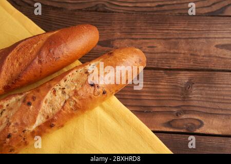 Due baguette croccanti francesi mentono tovaglioli di stoffa gialla tabella di legno baguettes di fondo in assortimento con semi di sesamo dolci classici nazionali francesi Foto Stock