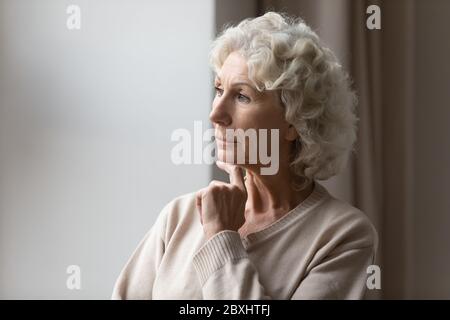 Triste donna anziana guardare in finestra pensare Foto Stock