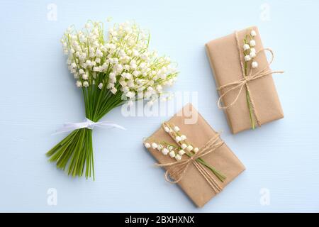 Bouquet di fiori giglio della valle e due scatole regalo carta kraft avvolto su tavolo blu, vista dall'alto. Regali per il giorno delle madri o per il giorno delle donne. Foto Stock