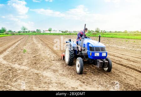 Un agricoltore che guida un trattore in un campo agricolo. Agricoltura e lavoro nel settore agricolo. Coltivando terreno di terra per piantare ulteriormente. Utilizzando la tecnologia Foto Stock