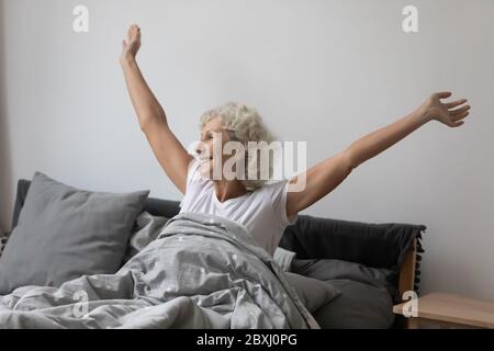 Donna matura felice svegliarsi in letto stretching Foto Stock