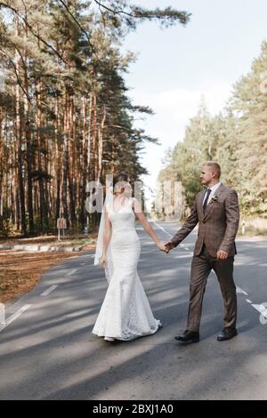 Sposa e sposo che si dirigono sulla strada nella foresta tenendolo le mani l'un l'altro. Ritratto di sposa e sposo Foto Stock