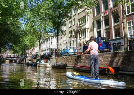 Uomo su un SUP (stand-up paddle board) sui canali nel centro della tranquilla Amsterdam (Paesi Bassi) durante la crisi del Covid-19 Foto Stock