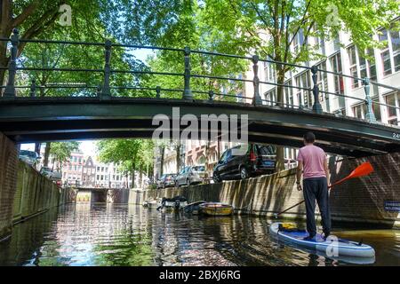 Uomo su un SUP (stand-up paddle board) sui canali nel centro della tranquilla Amsterdam (Paesi Bassi) durante la crisi del Covid-19 Foto Stock
