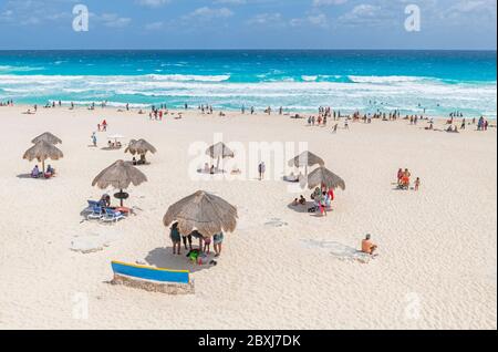 Turisti e messicani su Playa Delfines sotto ombrelloni a canna vicino al Mar dei Caraibi, Cancun, Penisola dello Yucatan, Messico. Foto Stock