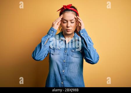 Giovane bella donna bruna che indossa camicia casual denim e fazzoletto capelli con mano sulla testa per il dolore alla testa perché lo stress. Soffrire di emicrania. Foto Stock