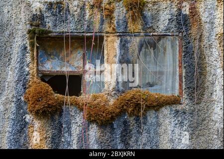 La vecchia finestra è marcio in una stazione di pompaggio con la crescita di muschio e le striature d'acqua sul muro della casa. Foto Stock