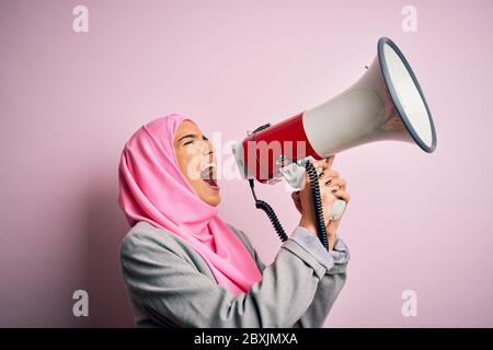 Business arab donna indossare hijab gridando arrabbiato per protesta attraverso il megafono. Urlando eccitato sulla conversazione ludspeaker e urlando le notizie Foto Stock