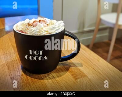 Bella tazza di cioccolata calda con crema fresca e marshmallows su panca di legno nel Cafe, UK Foto Stock