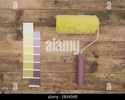 Rullo di vernice e tavolozza dei colori su sfondo di legno. Foto Stock