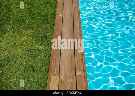 Piscina d'acqua pulita con terrazza in legno e erba verde intorno. Foto Stock