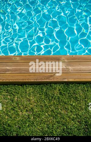 Piscina d'acqua pulita con terrazza in legno e erba verde intorno Foto Stock