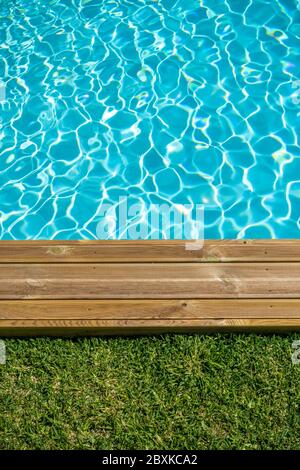 Piscina d'acqua pulita con terrazza in legno e erba verde intorno Foto Stock