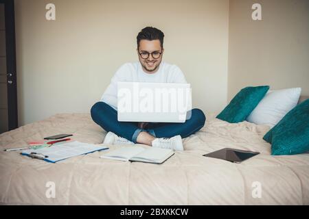 Felice studente caucasico seduto sul divano e avendo lezioni online mentre si usa un portatile e libri Foto Stock