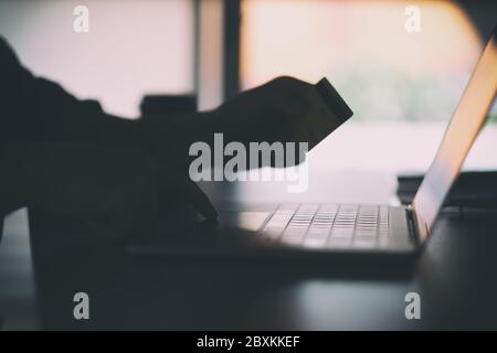 Immagine di silhouette di un uomo d'affari che utilizza un computer portatile e una carta di credito per lo shopping online Foto Stock