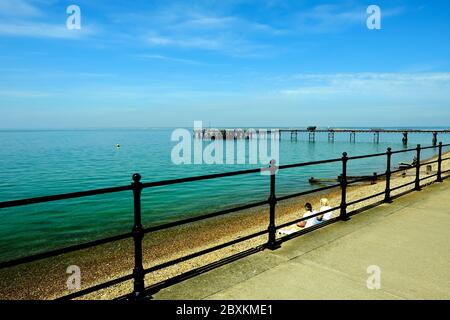 Totland Bay lungomare Isola di Wight che mostra il vecchio vittoriano pier che guarda fuori attraverso il Solent verso la terraferma due donne in spiaggia Foto Stock