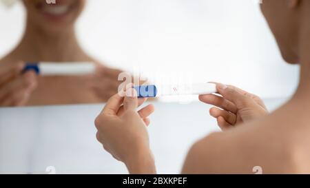 Primo piano sorridente donna che tiene un test di gravidanza con due linee Foto Stock