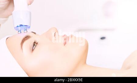 Procedura di estetica della luce microcorrente. Bellezza faccia ragazza. Macchina cosmetologica. Mani del medico. Due micro sfere. Riduzione delle rughe Foto Stock