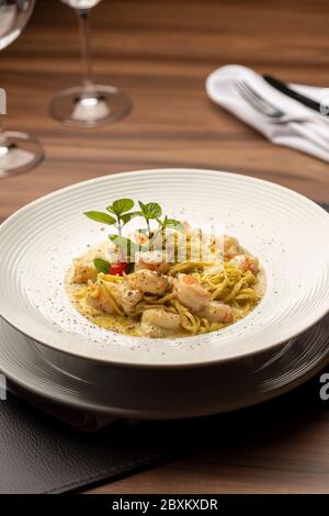 Gamberi cremosi pasta italiana su piatto e tavolo in legno, tappeto in pelle di tovagliolo forchetta e bicchieri da vino Foto Stock