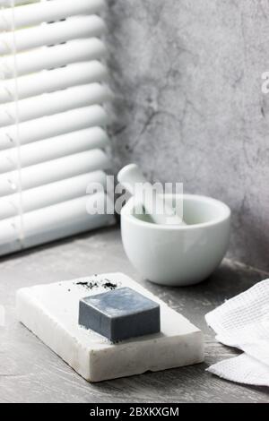 Sapone fatto a mano con carbone attivo su marmo, polvere di carbonio e un asciugamano di cotone su fondo grigio. Foto Stock